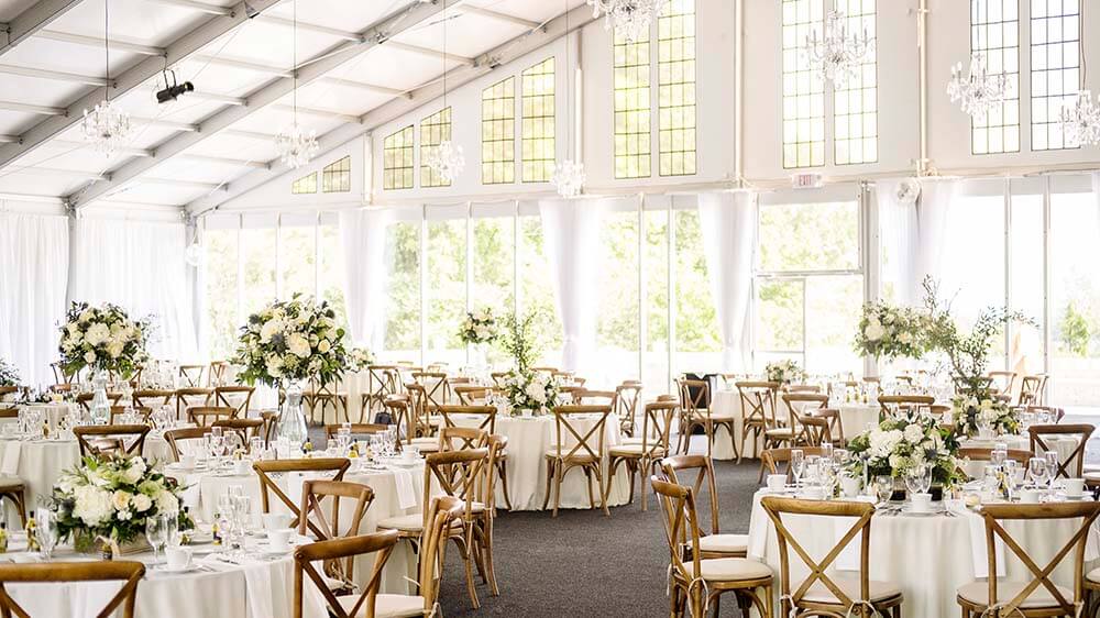 Wedding Structure Tent Interior — Chandeliers & Floral Design Elegant wedding structure tent interior with crystal chandeliers, white florals, cross-back chairs, and glass window walls