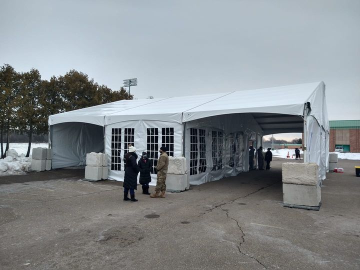 Drive-through emergency response tent deployed in winter with military personnel and concrete barriers for vaccination operations