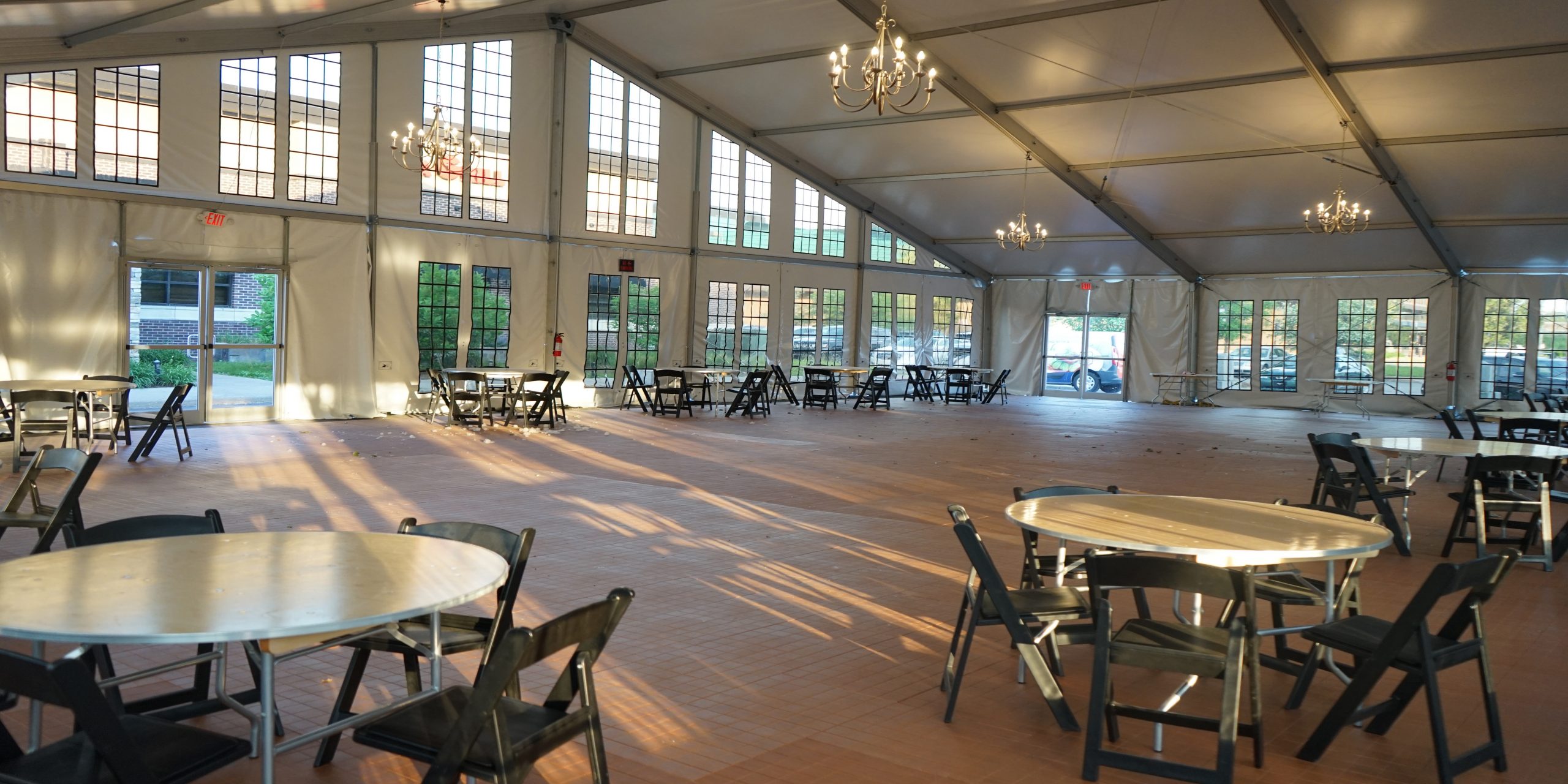 Elegant clearspan structure interior with chandeliers, windowed walls, hardwood flooring, and banquet seating for dining events