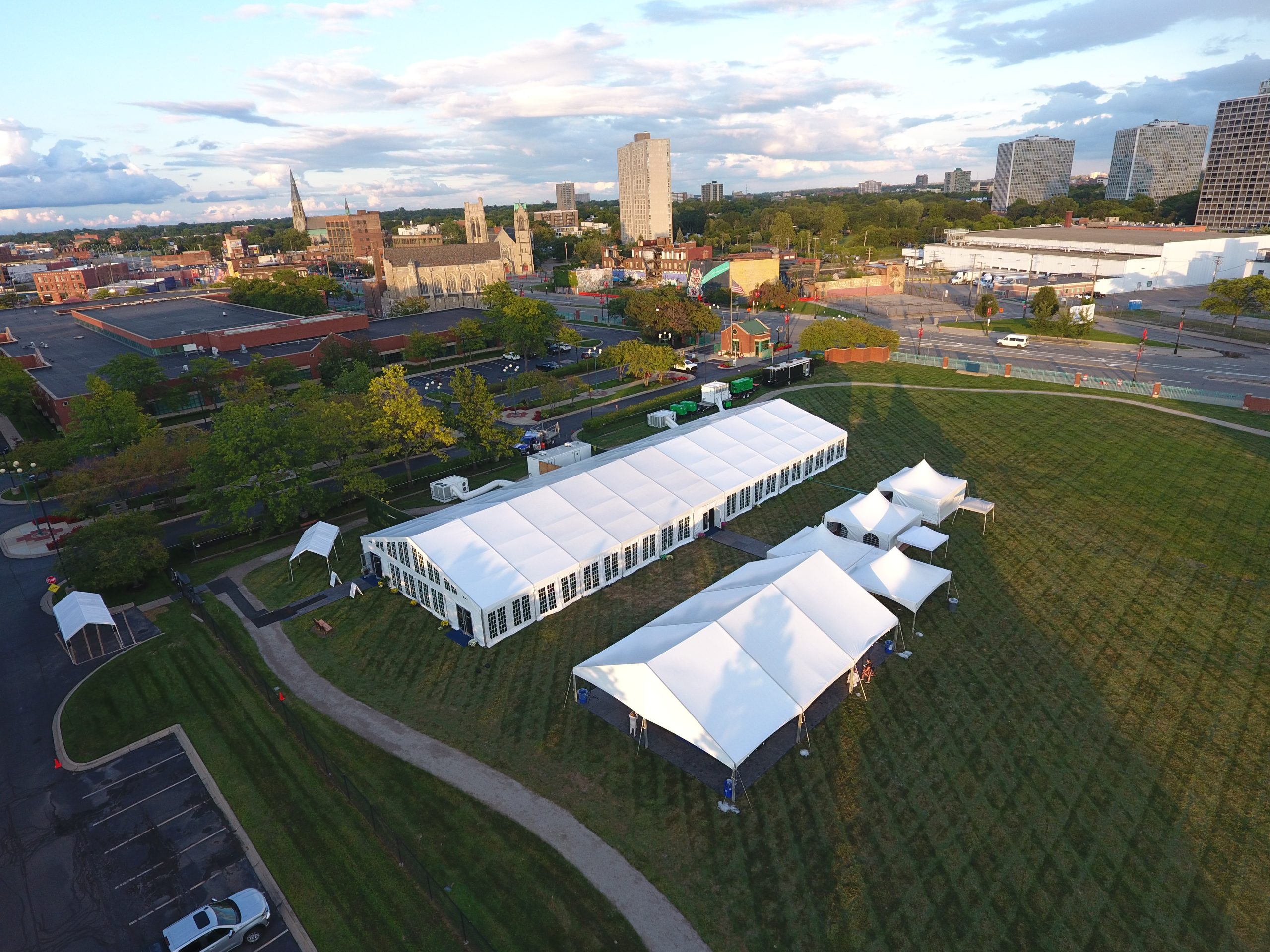 Wide aerial view of base camp tent campus with main structure, dining tents, and support facilities with city skyline