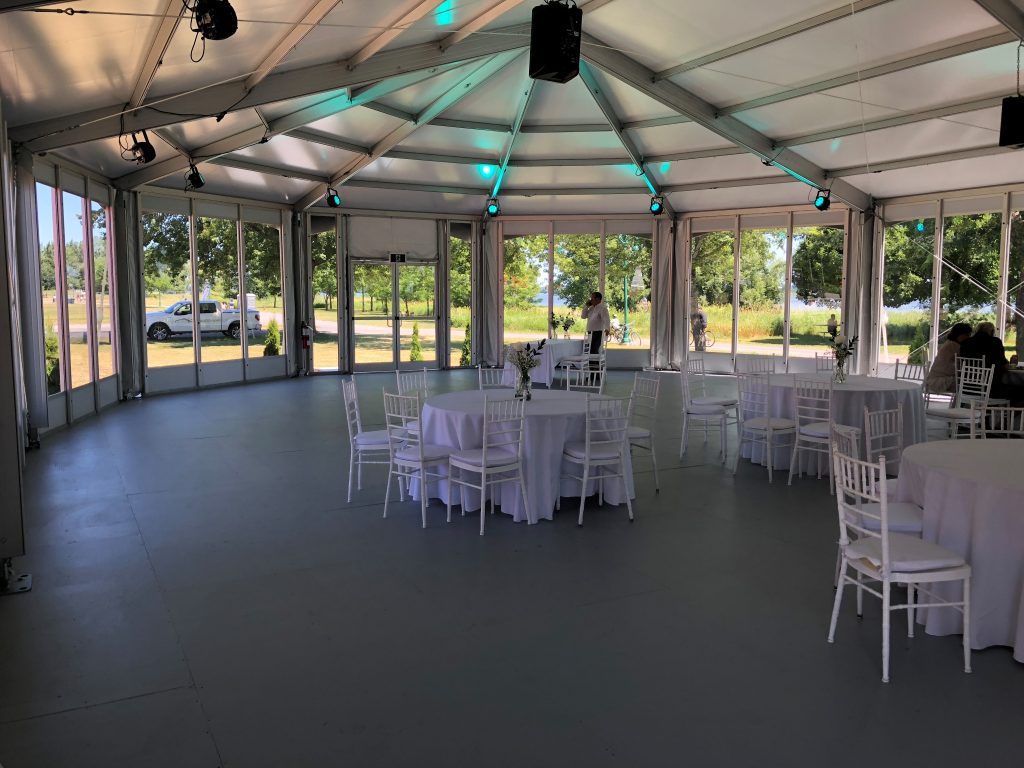 Glass-Walled Structure Tent Interior for Weddings Structure tent interior with floor-to-ceiling glass wall panels, round tables, and chiavari chairs for wedding reception